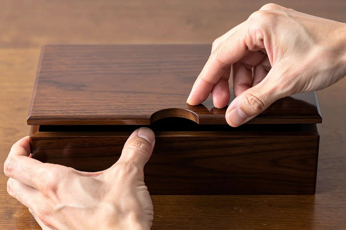 Hands steadying a wood-grain box and lifting its lid near the front finger recess