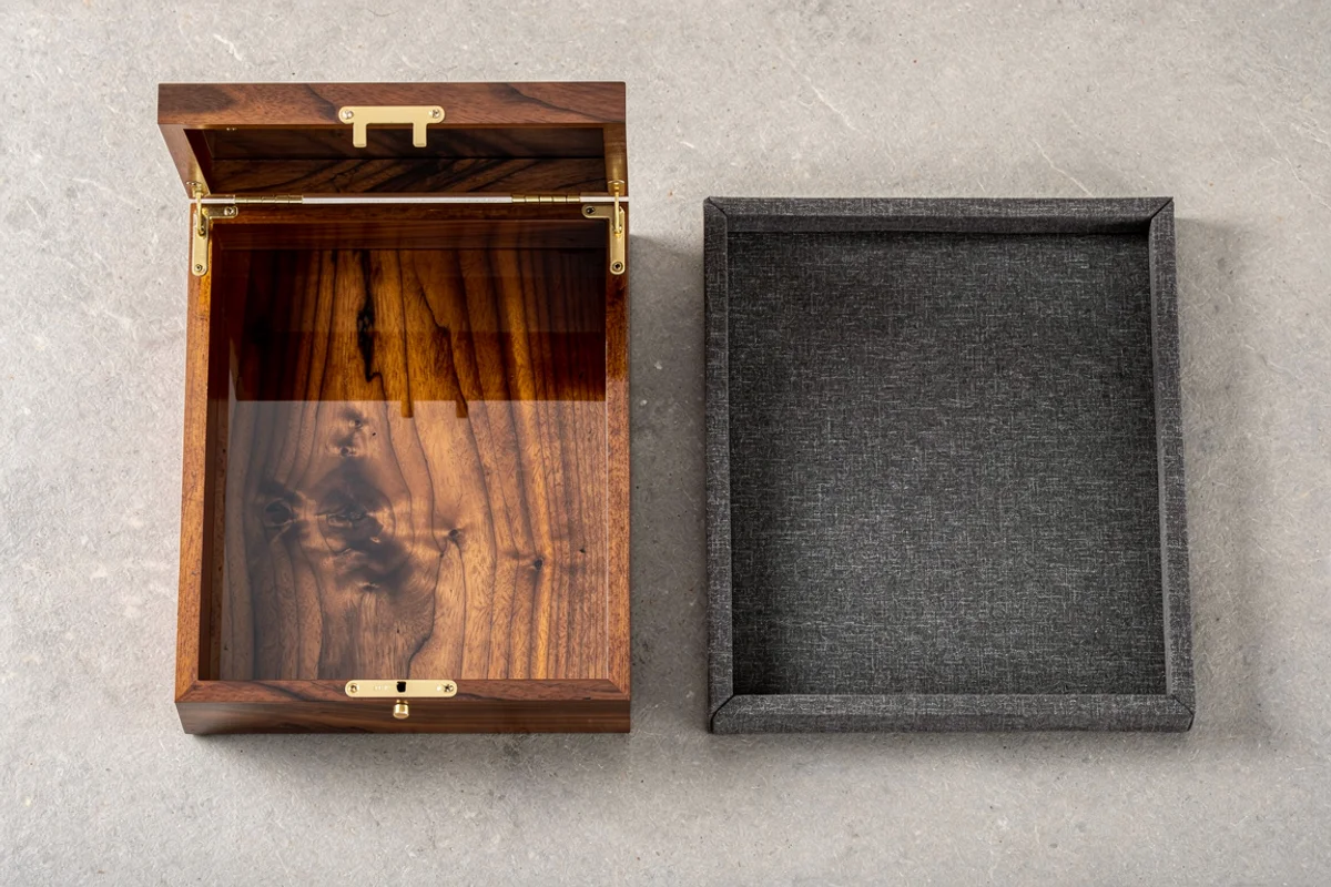 Overhead view of an open lacquered wooden box and a separate fabric-covered tray