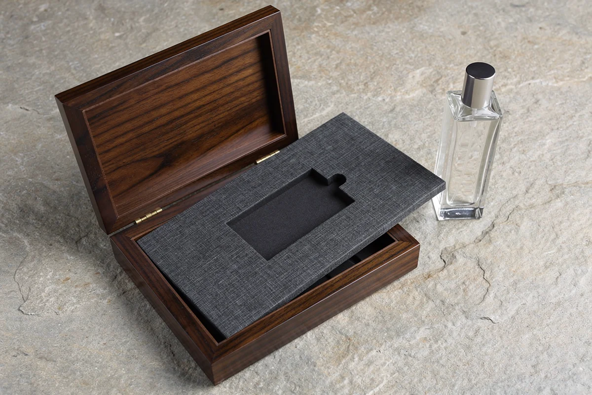 Fabric-covered insert resting across an open wooden box beside a glass bottle