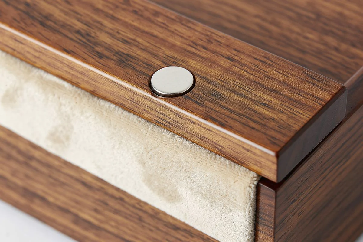 Round silver closure disc on a finished wooden box rim beside cream lining