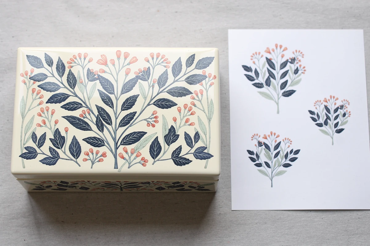 Ivory wooden box with fine multicolour botanical lid decoration beside a printed sheet