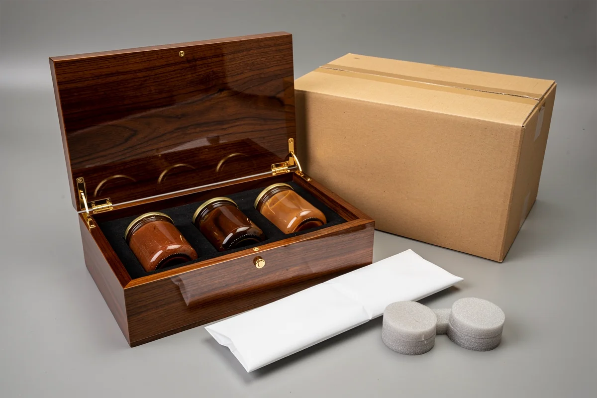 Open lacquered wooden box with three capped glass jars beside a carton and separate protective materials